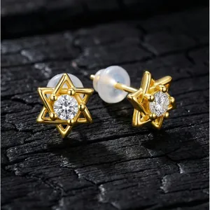 Gros plan de puces d'oreilles hexagrammes plaquées or avec zircons sur bois sombre.