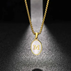 Macro view of the gold-plated oval pendant featuring a white shell inlay and 'M' initial detail.