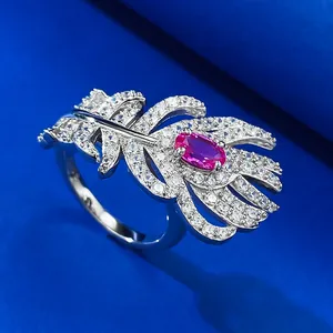 Close-up of a silver feather ring with pave diamonds and a central pink gemstone.