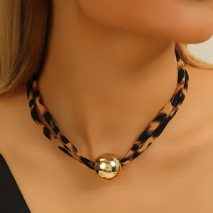 Primo piano di un choker in tessuto leopardato con un grande ciondolo a sfera dorata