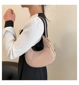 Side view of a chic beige crocodile pattern crescent underarm bag worn by a model