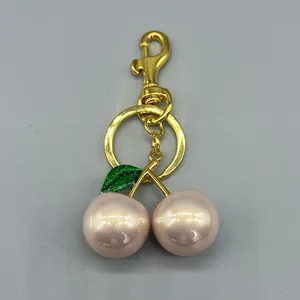Detailed view of the cherry-shaped bag charm with pink pearl finish spheres and golden hardware.