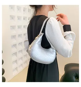 Silver croc-embossed crescent shoulder bag shown on model in modern interior.