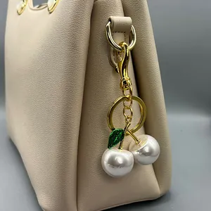 Macro view of elegant pearl cherry bag charm with green leaf on beige leather purse