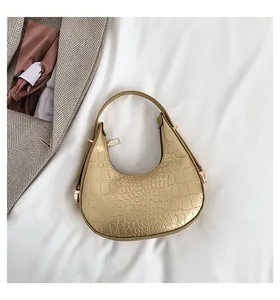 Detail of a golden crocodile-embossed crescent hobo bag on white fabric background.