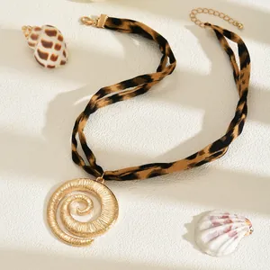 Dettaglio di una collana in tessuto leopardato con un ciondolo a conchiglia a spirale d'oro.