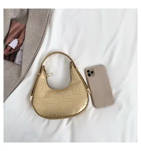 Detail of gold croc-embossed moon hobo bag showing size scale with a smartphone.