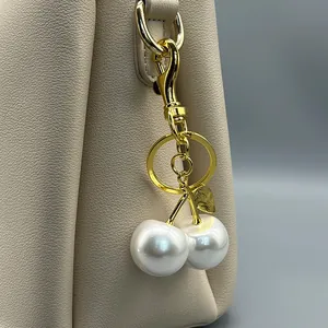 Close-up detail of a luxury pearl cherry bag charm attached to a beige leather bag.
