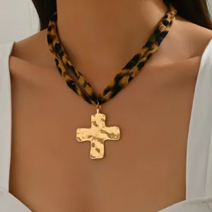 Dettaglio del ciondolo a croce dorata martellata su collana a doppio cordino leopardato