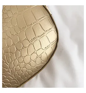 Detailed macro shot showing the golden crocodile embossed texture of the crescent bag