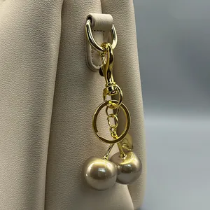 Close-up view of a luxury golden cherry bag charm hanging on a beige leather handbag