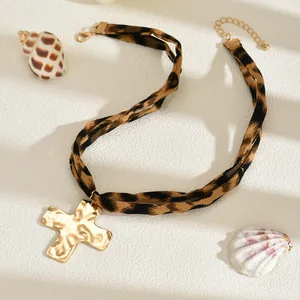 Dettaglio della collana choker leopardata con pendente a croce in oro martellato.