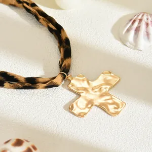 Primo piano del ciondolo a croce in oro martellato con collana in tessuto leopardato.