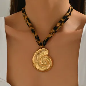 Dettaglio di una collana con ciondolo a conchiglia dorata con cordino in tessuto leopardato