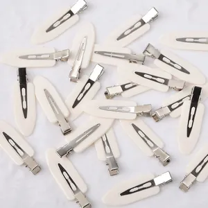 Detail view of cream-white no-trace duckbill hair clips on white plush background
