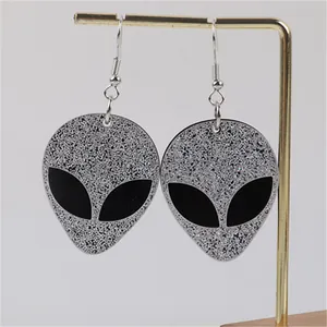 Detailed view of glittery silver alien head drop earrings displayed on a gold stand