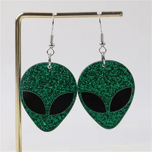 Close-up of green glittery alien head earrings on a golden display stand.
