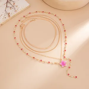 Gros plan d'un collier doré multi-rangs avec pendentif fleur rose et cristaux rouges