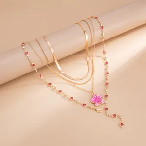 Gros plan d'un collier doré multicouche avec fleur en émail rose et cristaux rouges