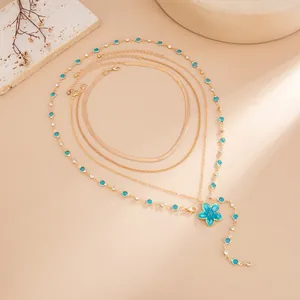Détail du collier multi-rangs doré avec pendentif fleur en émail bleu et cristaux