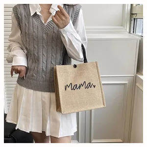 Woman holding a beige burlap tote bag with mama heart print, detail view