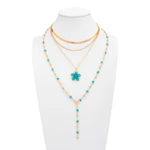 Détail d'un ensemble de colliers dorés multicouches avec fleur en émail bleu et cristaux