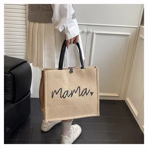 Close-up detail of a burlap tote bag featuring black 'Mama' script and heart print