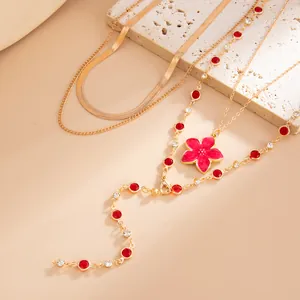 Gros plan d'un collier doré multicouche avec cristaux rouges et pendentif fleur rose.