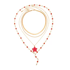 Parure de colliers dorés à plusieurs rangs avec pendentif fleur en émail rouge.