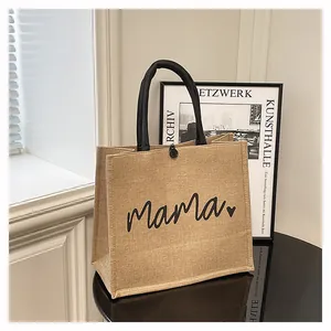 Close-up detail of a textured burlap tote bag with 'mama' print and black handles