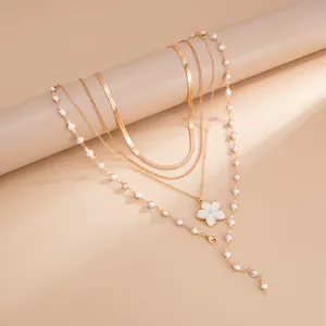 Détail d'un collier doré multi-rangs avec pendentif fleur blanche et perles