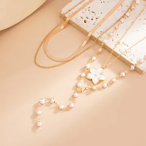 Détail de colliers dorés à plusieurs rangs avec fleur émaillée blanche et perles.