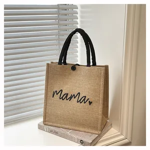 Close-up of burlap tote bag with Mama print and black handles on a white ledge