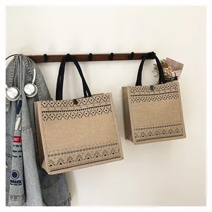 Close-up detail of jute burlap tote bags with black geometric patterns on a wooden hook rack