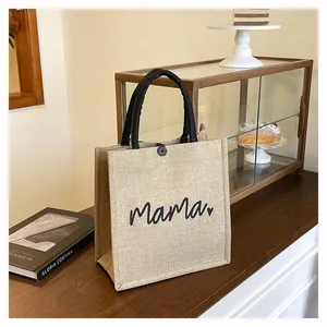 Detail view of a textured burlap tote bag with black handles and mama print.