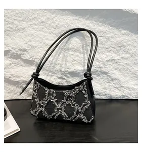 Close-up view of a stylish denim underarm baguette bag with frayed diamond patterns