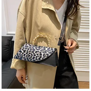 Leopard print crossbody bag with gold metal handle worn with a beige trench coat.