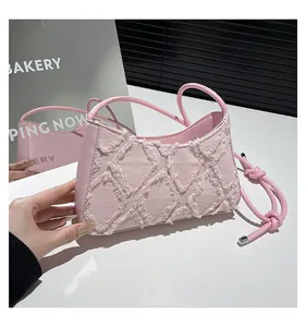 Macro view of pink denim underarm bag featuring frayed diamond stitching and knot detail