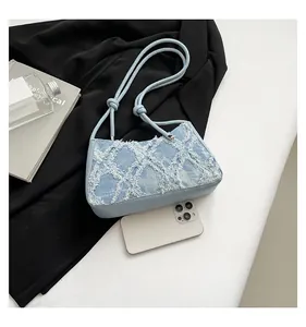 Detail of denim underarm bag with distressed lattice pattern and fringed texture.