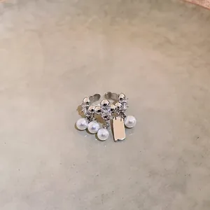 Detailansicht eines silbernen offenen Rings mit hängenden Perlen und Metallanhänger