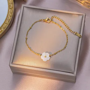 Dettaglio di un bracciale in acciaio dorato con un delicato fiore in madreperla bianca