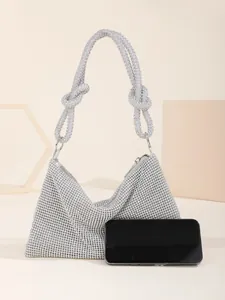 Silver rhinestone evening bag with knotted strap shown next to phone for scale