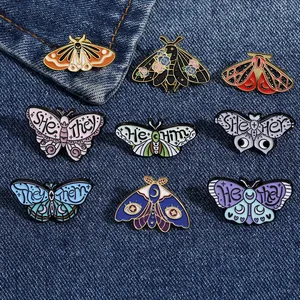 Detailed view of various butterfly and moth enamel pins with gender pronouns on denim.