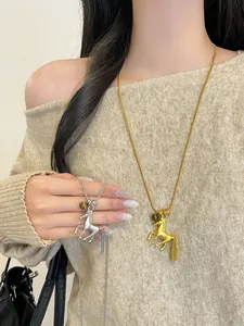Close-up of gold and silver horse pendant necklaces worn on a soft beige knit sweater.