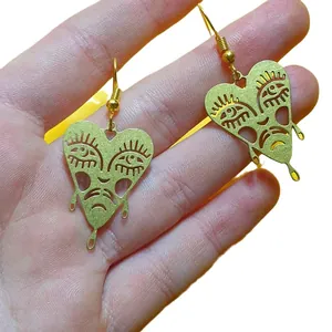 Hand-held close-up of unique brass heart earrings featuring a crying melting face design