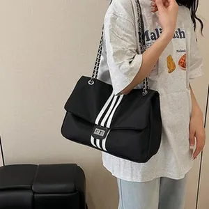 Detail of black shoulder bag with three white stripes and chain strap