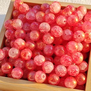 Close-up of red water-dyed glass beads with gold flecks in a wooden tray.