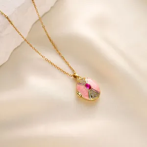 Close-up of a gold locket necklace featuring pink enamel and a red central gemstone