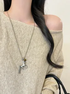 Detail of a silver metal horse pendant necklace with tassel and bead on a beige sweater.