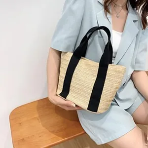 Detailed view of the casual woven straw tote bag with black canvas straps worn by a model